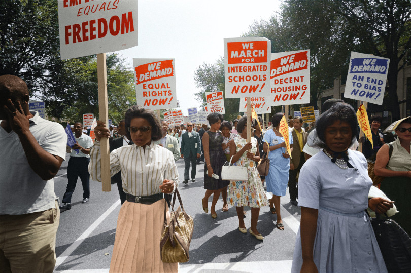 A group of people marching down the street holding signs.