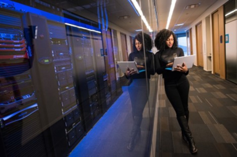 A woman standing in front of a wall with two laptops.