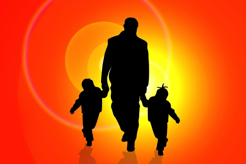 A man and two children walking in front of an orange background.