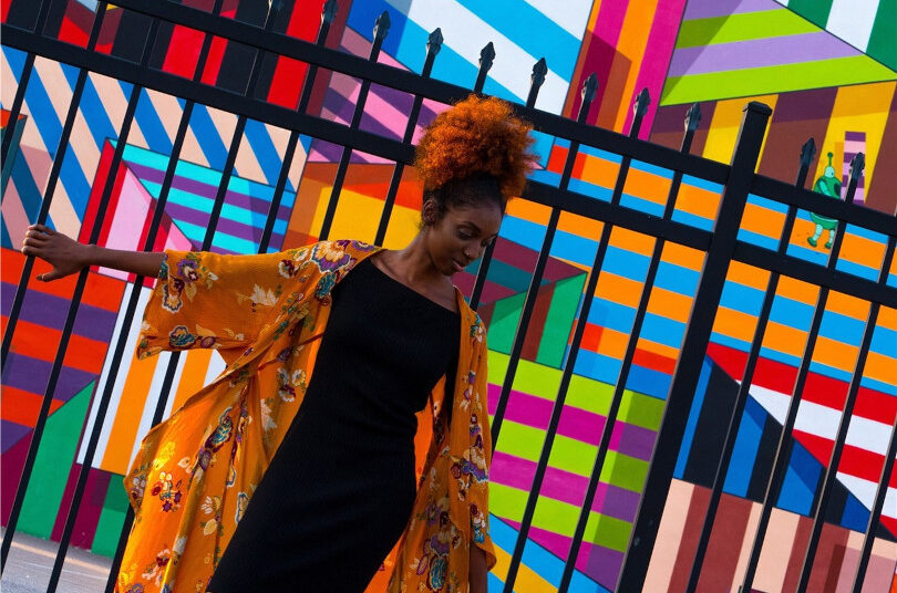 Woman in vibrant clothing by colorful mural.