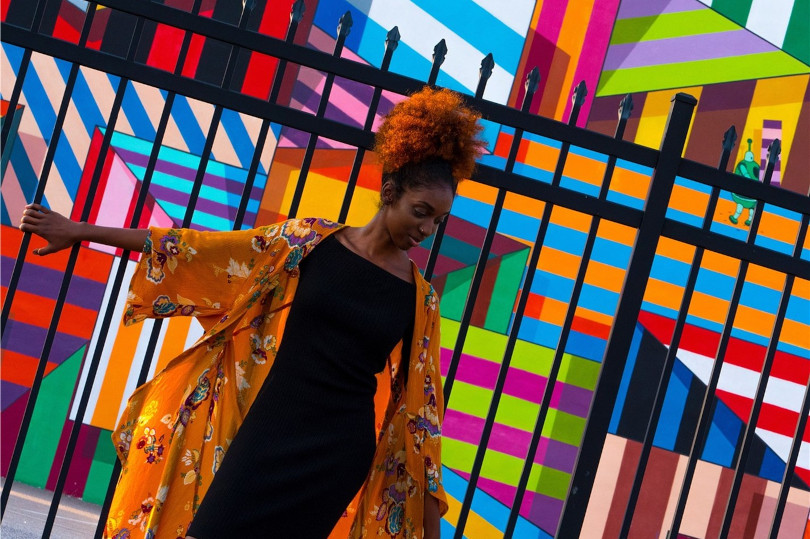 Woman in vibrant clothing by colorful mural.