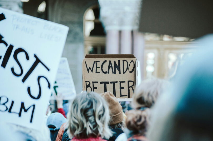 Protest signs with "We Can Do Better.